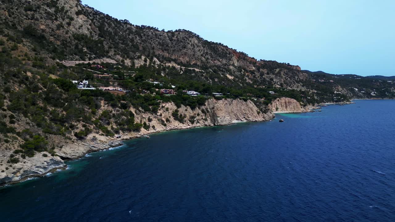 Aerial view of boats mooring near a rocky coast with lush vegetation in Ibiza, Spain. Majestic aerial view flight panorama overview drone