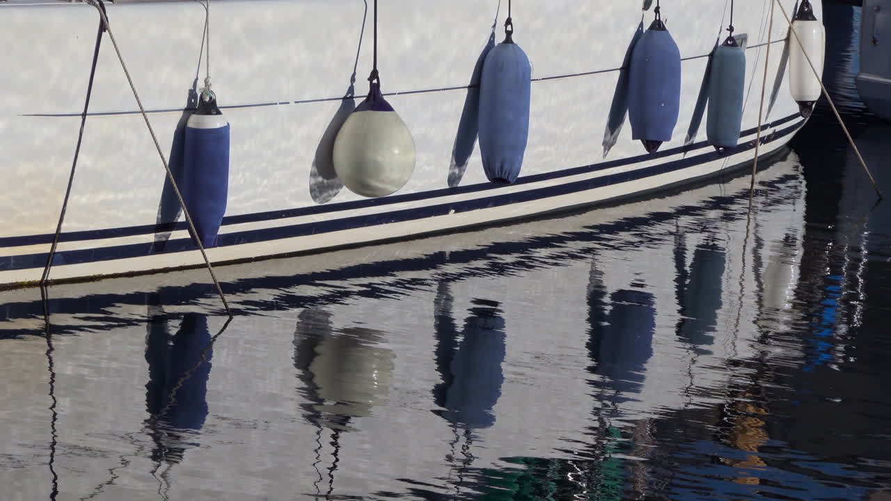 Close up of the side of a boat docked in the water, with fenders hanging from its hull