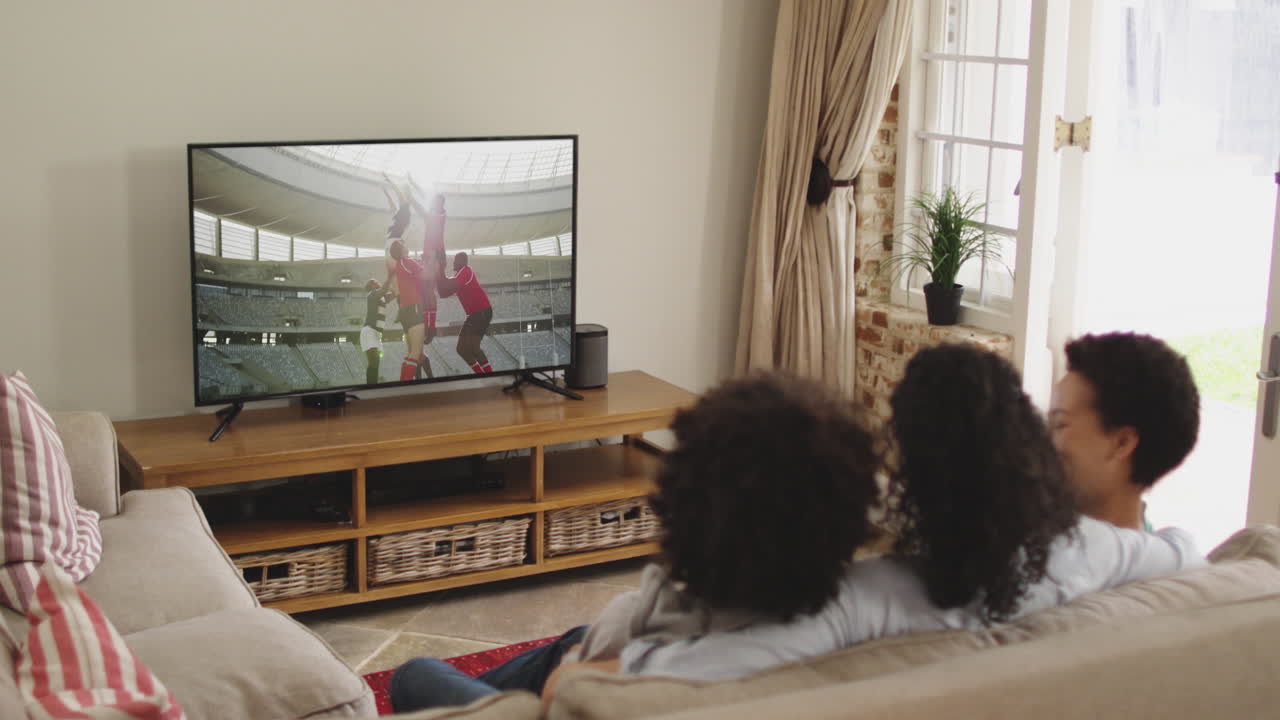 Famiglia felice seduta a casa insieme che guarda una partita di rugby in TV
