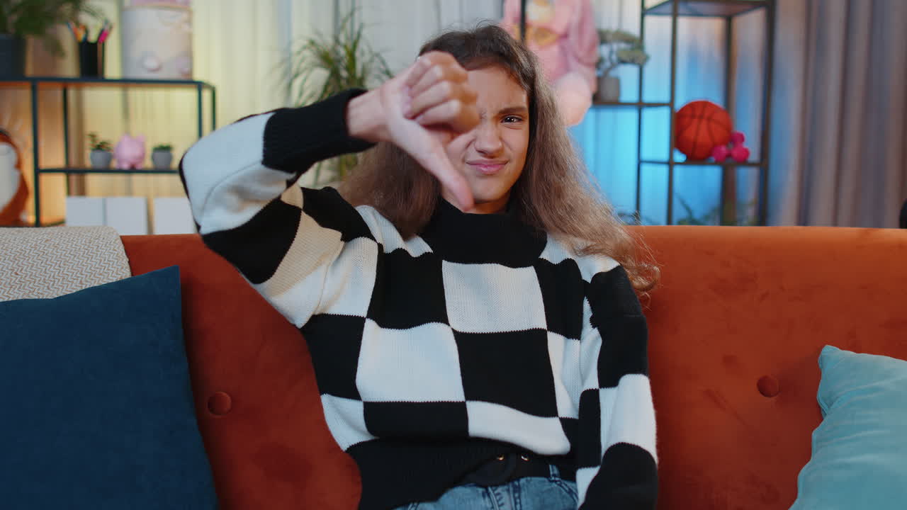 расстроенная молодая девушка, показывающая пальцы вниз, не нравится плохая работа, неодобрение, неудовлетворенная обратная связь дома