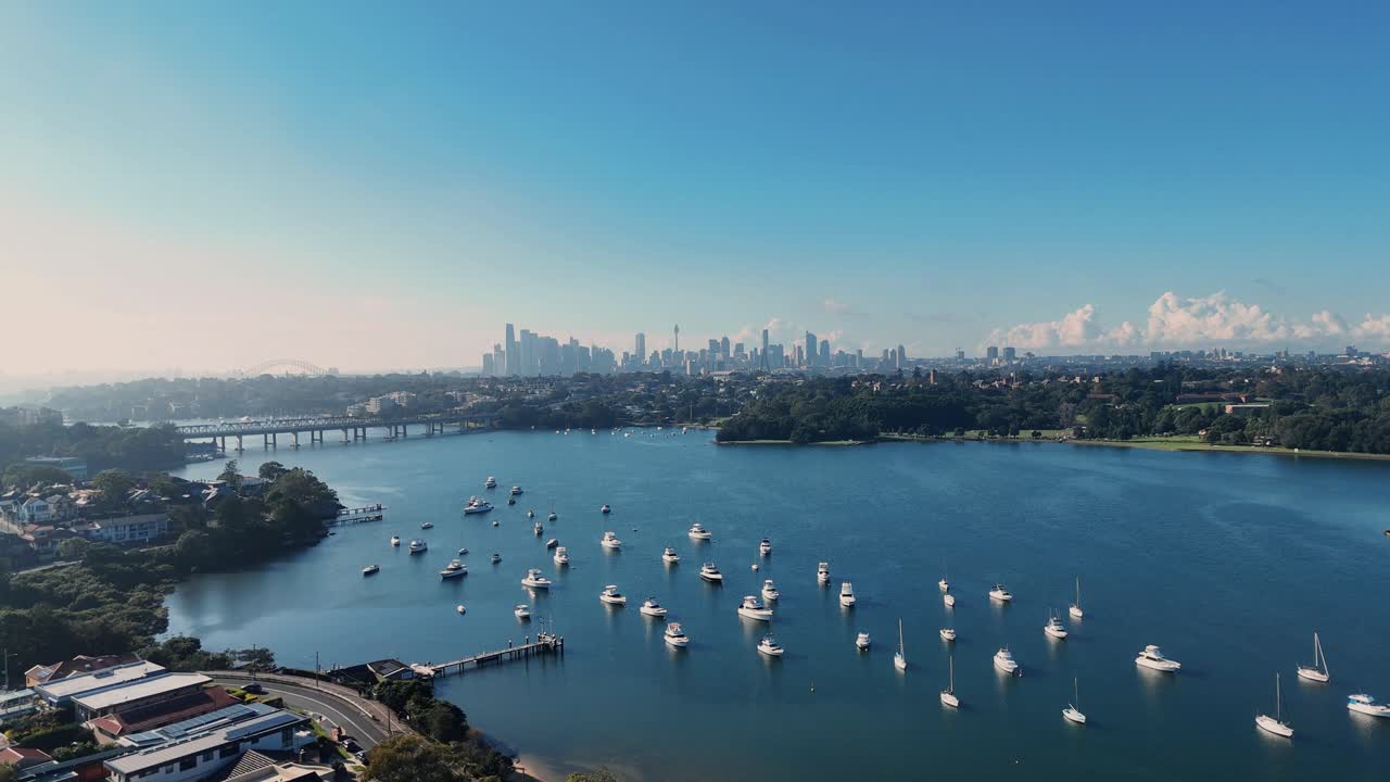Aerial establishing pullback above luxury boats anchored in water, Drummoyne Sydney Skyline in distance