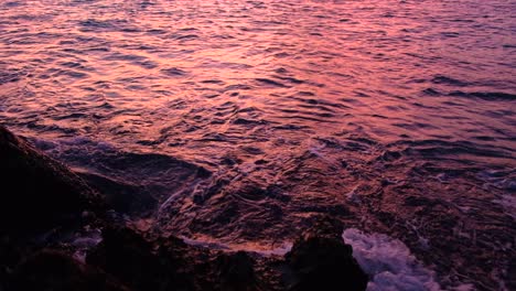 ripply ocean waves reflecting beautiful sunset colors and hitting on rocks, medium shot