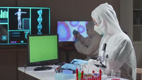 asian doctor in protective suit working with mock up green screen computer display in a modern lab. laboratory assistant workplace