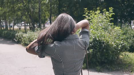 backside view brunette girl walking in park fixes long hair