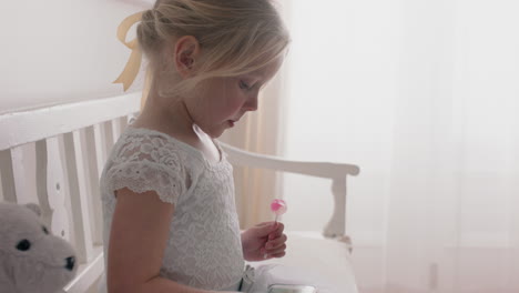 beautiful little girl using smartphone watching online entertainment sitting on bench with teddy bear eating lollipop at home 4k footage