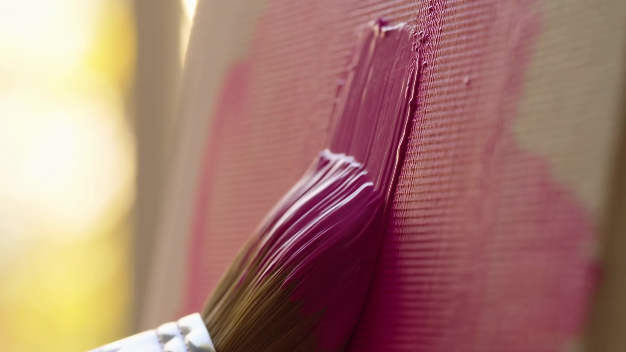 Un primissimo piano mostra un pennello rotondo che trascina vernice magenta lucida su una tela tessuta, con setole compresse, lucentezza bagnata, superficie texturizzata e un bordo di vernice in rilievo sotto una retroilluminazione calda per scopi creativi.