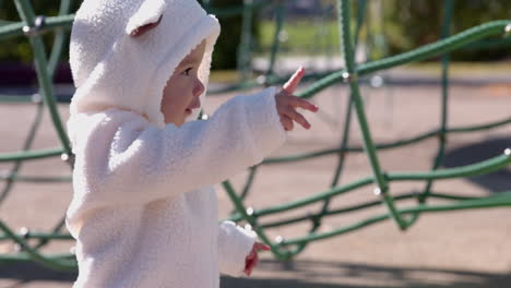 toddler girl bundled up explores outdoor play structure park on sunny cold autumn day - side profile