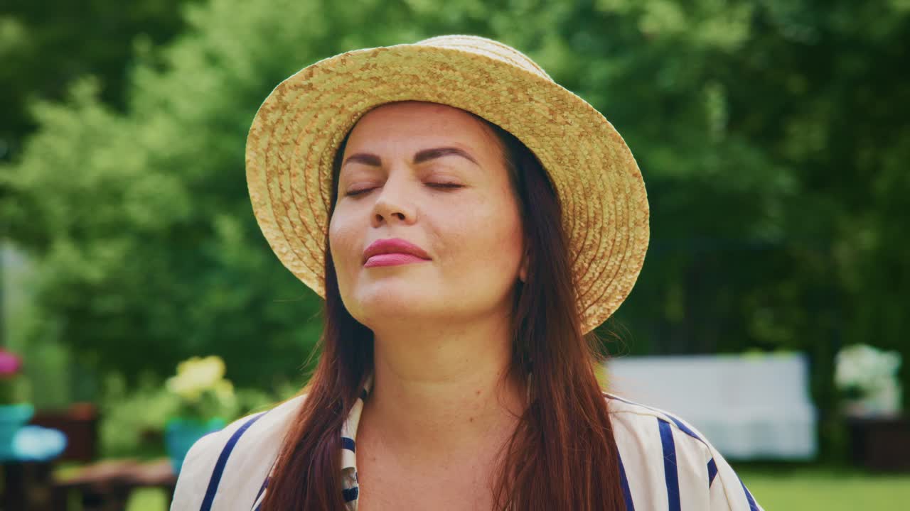 Woman with long hair wearing straw hat enjoying nature in a sunny outdoor garden setting
