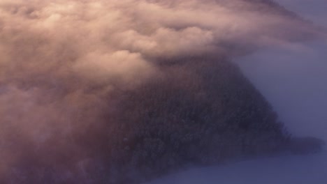 Flying-over-fog-mist-clouds-and-frost-covered-seasonal-forests-in-sunrise-light