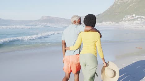 happy african american couple walking and embracing on sunny beach