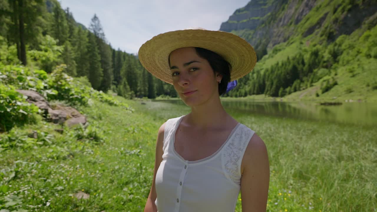 Woman in white dress and sunhat enjoys peaceful summer day by a mountain lake surrounded by trees