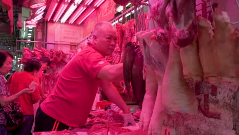 at the bustling hong kong fresh market, a skilled butcher prepares pork cuts for a line of waiting customers.