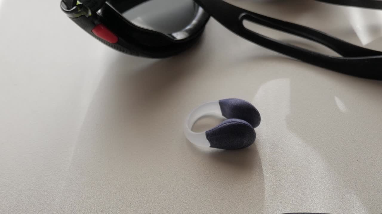 Close-up of black swimming goggles and silicone nose clip on white surface under soft daylight