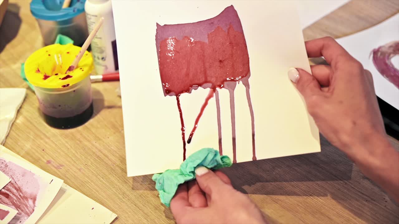 A woman in a studio painting on paper with red wine and wipe, close view, slow motion