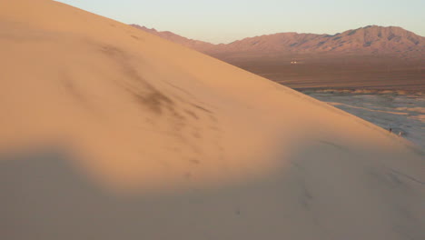 Aerial-of-two-people-climbing-a-huge-sand-dune-in-the-desert