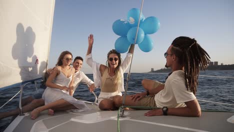 Four-friends-having-relaxing-cruise-on-the-yacht-while-lying-on-a-bow-of-the-boat.-They-enjoying-the-moment---girl-in-a-white-waving-the-balloones,-celebating.-Slow-motion