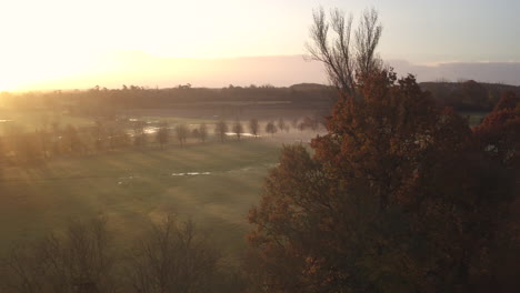 slow aerial drift over autumnal treetops with a beautiful sunrise glow over the landscape, long shadows and mist