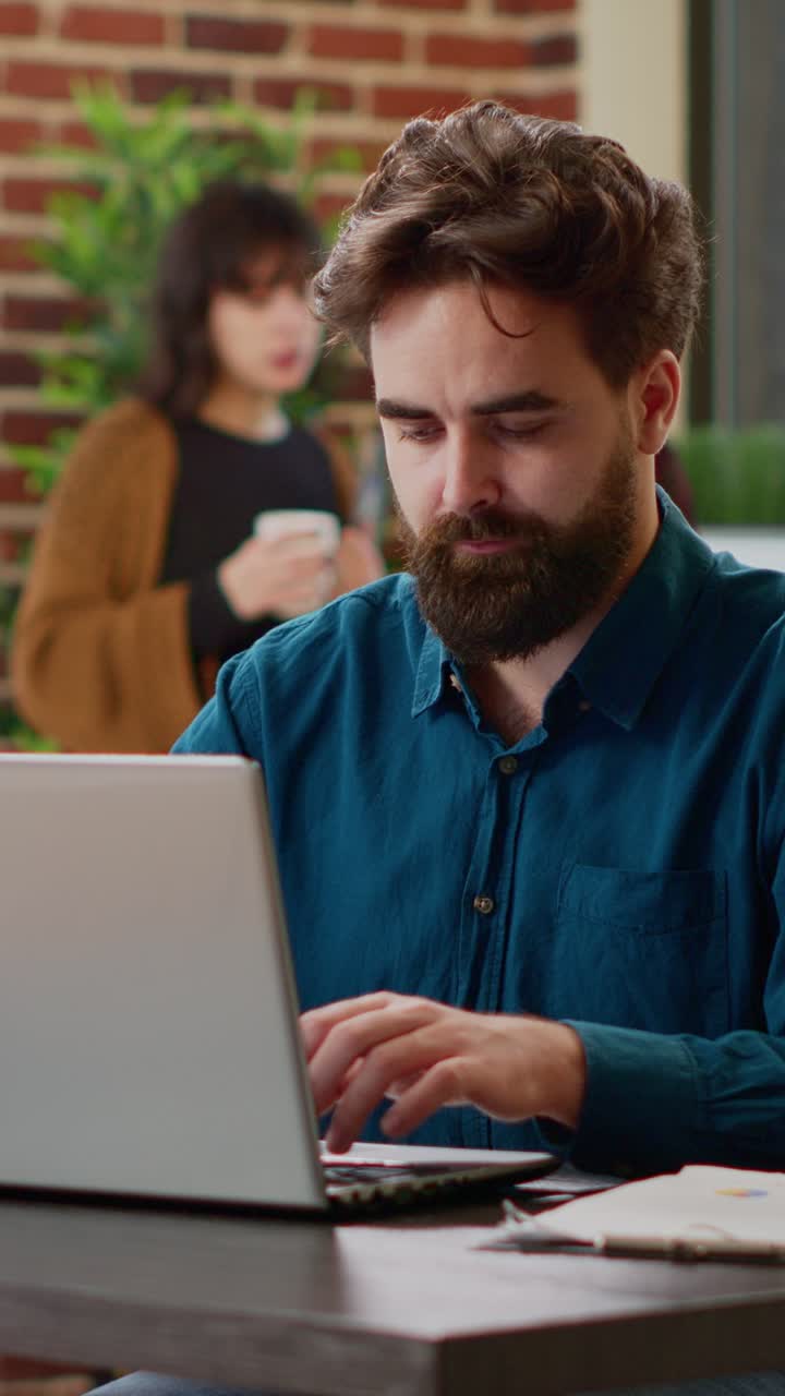 Man working on laptop with woman in background