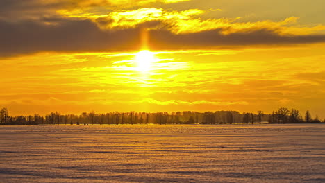 Sun-rises-high-into-sky-illuminating-a-white-snow-landscape-yellow,-clouds-rush-by