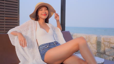 카메라에 포즈를 취하고 웃고 있는 바다 옆 해변 의자에 앉아 있는 아시아 여성의 슬로우 모션