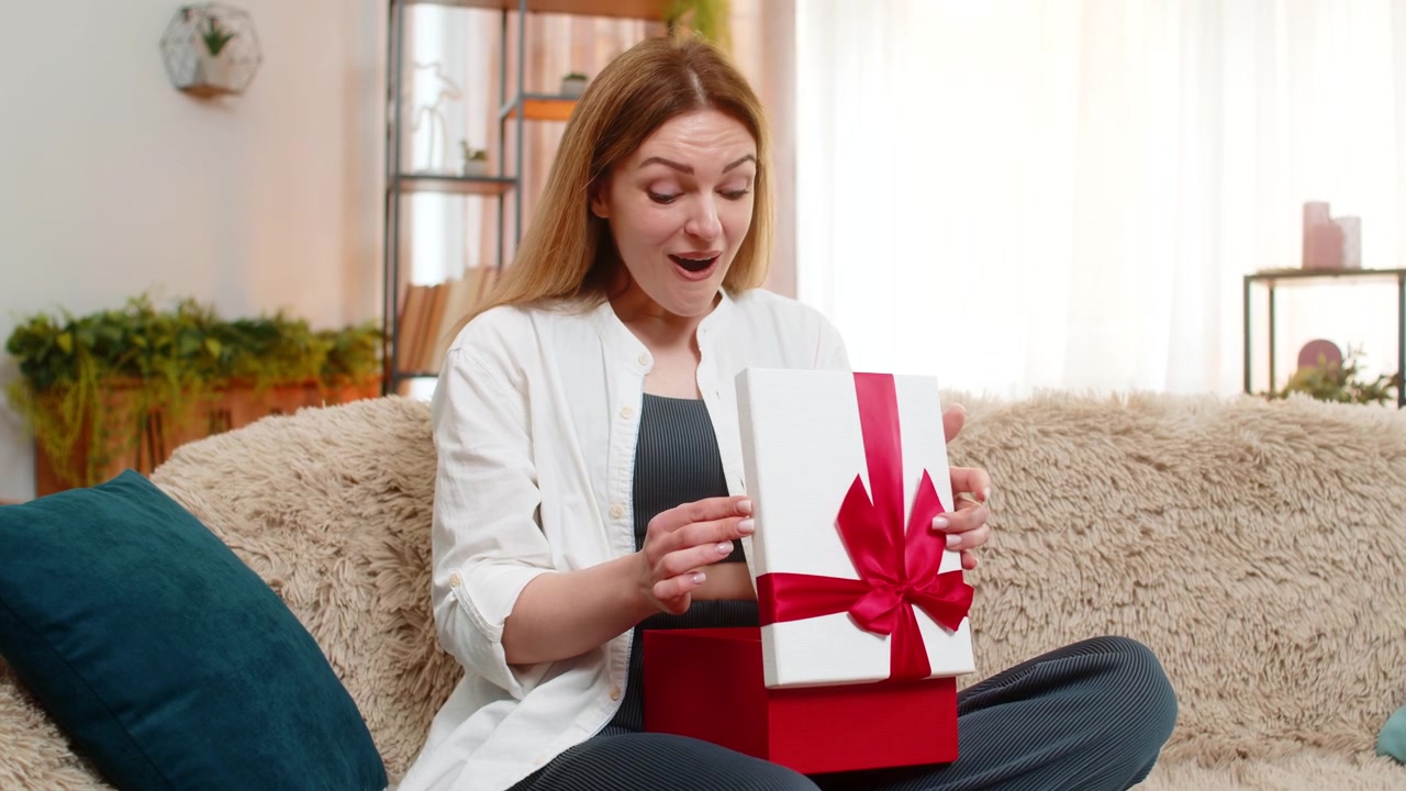 Adult woman opening gift at home smiling with excitement happiness surprised by thoughtful present