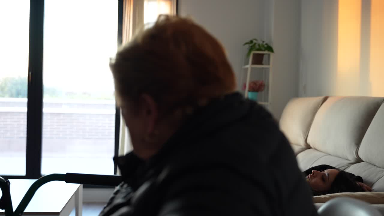 Pensive granny and tired granddaughter on the sofa at sunset. Rack focus