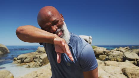 senior african american man exercising wiping his face on rocks by the sea