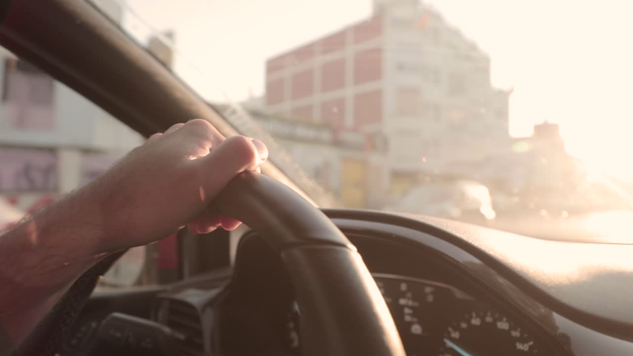 Slow motion, close up on person's hand steering car wheel during golden hour