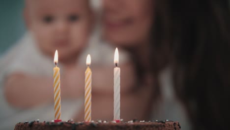 madre soplando tres velas en el pastel de cumpleaños del bebé. concepto de la fiesta de cumpleaños del bebé