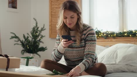 Mujer-Caucásica-Sentada-En-La-Cama-Y-Tomando-Fotografías-Con-Un-Teléfono-Inteligente-De-Regalos-De-Navidad-Envueltos