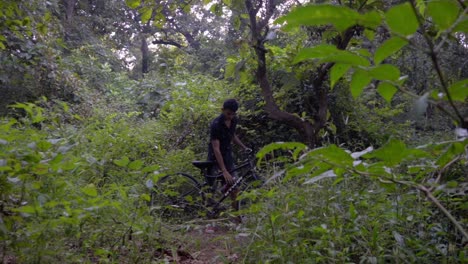 boy man walking with a cycle in deep jungle slow-motion drinking water