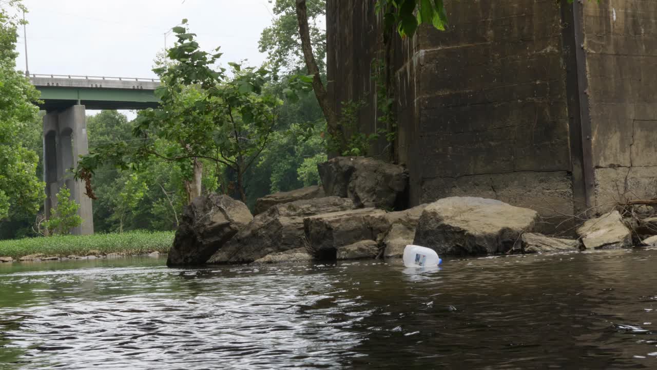 la jarra de leche flota río abajo lentamente hacia el viejo puente de hormigón en un día nublado de panorámica amplia