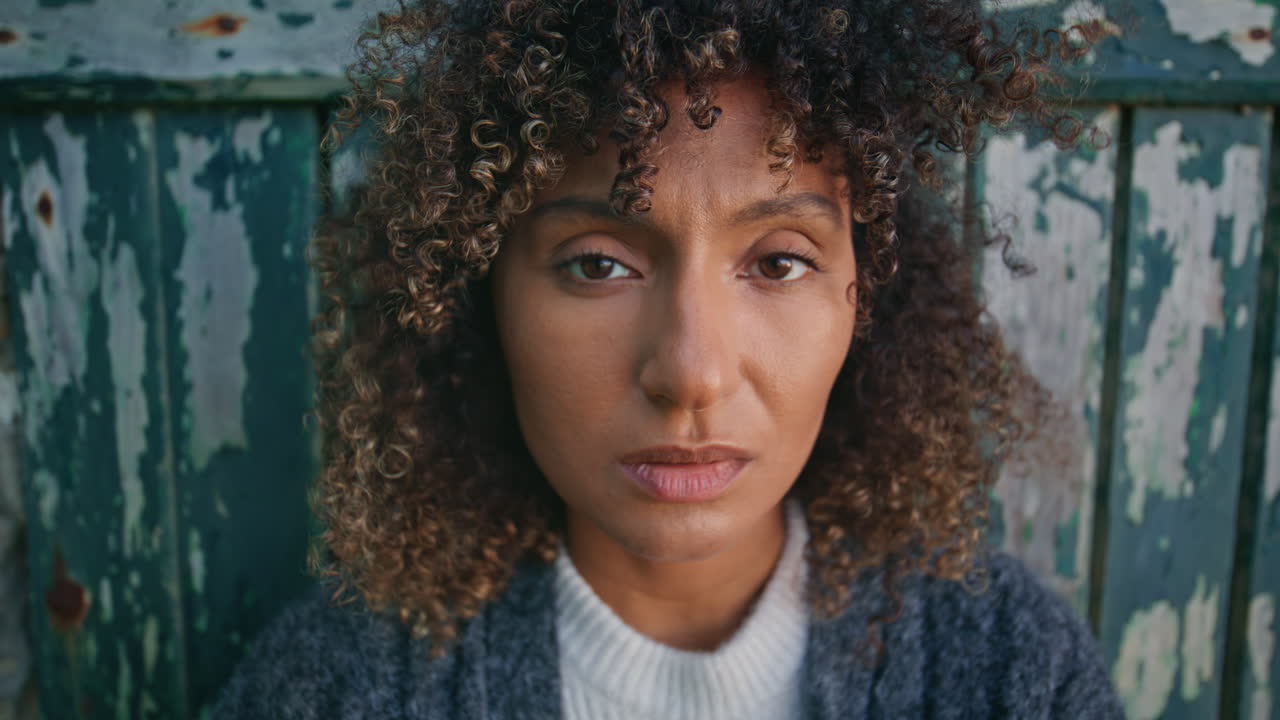 Sad woman posing door at windy day portrait. Curly tanned woman looking camera