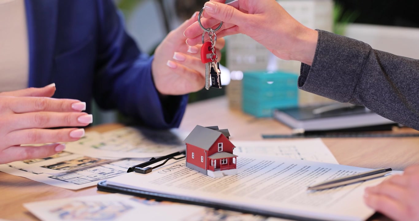 Un'agente immobiliare consegna la chiave della nuova casa al cliente in ufficio.