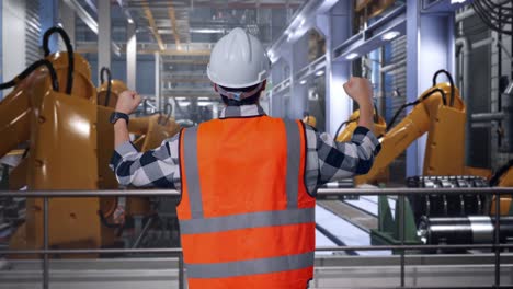 back view of a male engineer with safety helmet raising his hands celebrating while working with industrial robotic arms working
