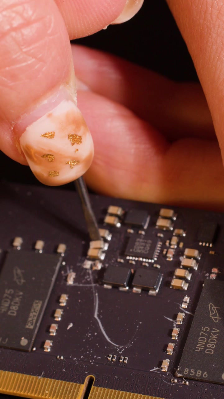 Macro shot of hand using metal tool to scrape components from a RAM memory module