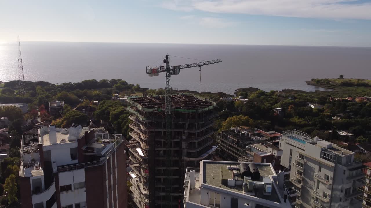 vista aérea de una grúa en la parte superior del techo de un edificio en construcción y el mar en el fondo, buenos aires en argentina