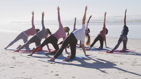 Multi-ethnic-group-of-women-doing-yoga-position-on-the-beach-and-blue-sky-background