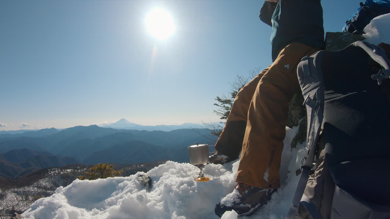 um homem fervendo água em uma montanha de inverno