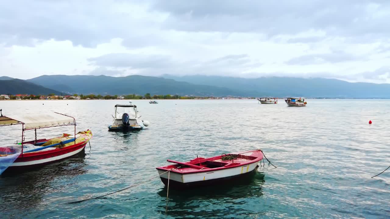Moored boats on the shore of the Aegean sea, town and hills on the background, cloudy sky in Stavros, Greece
