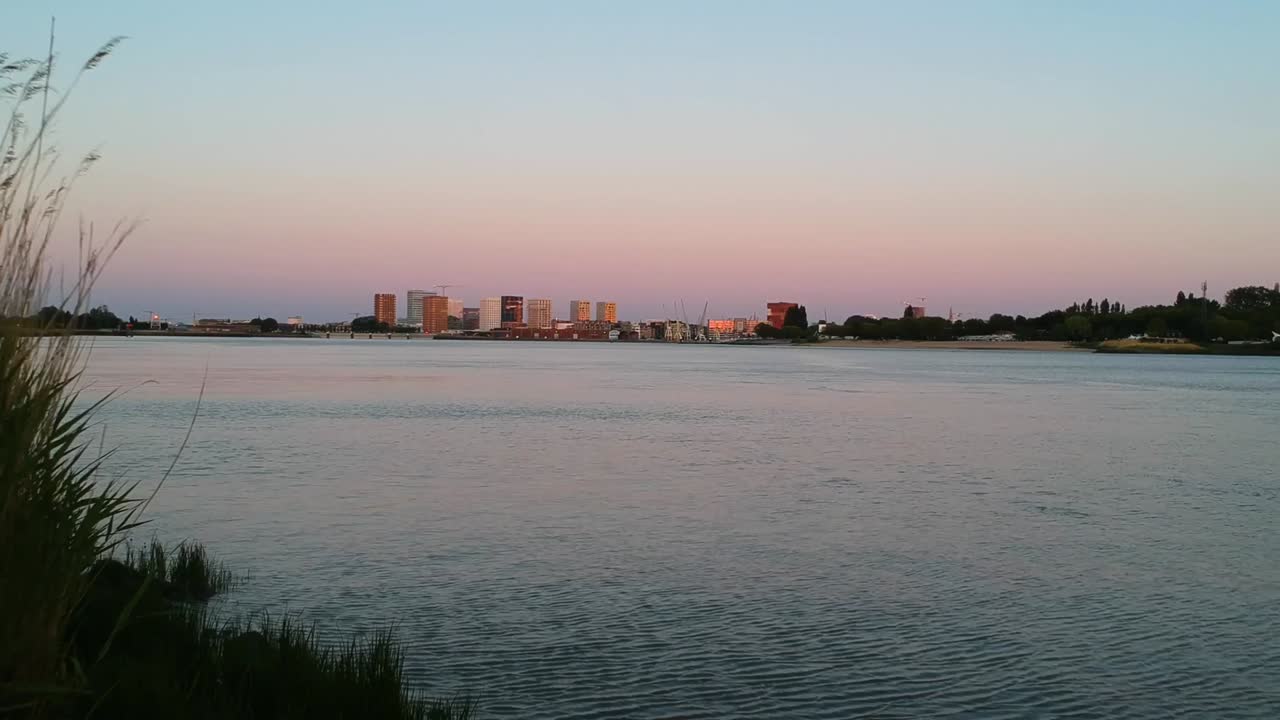 tiro de dron de empuje junto a las orillas del río con la ciudad de fondo filmado durante la hora dorada