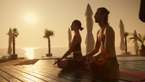 Ein-Paar,-Ein-Mann-Und-Ein-Mädchen,-Meditieren-Während-Eines-Goldenen-Sonnenaufgangs-Im-Sommer-Auf-Einem-Roten-Teppich-An-Einem-Mit-Brettern-Bedeckten-Strand