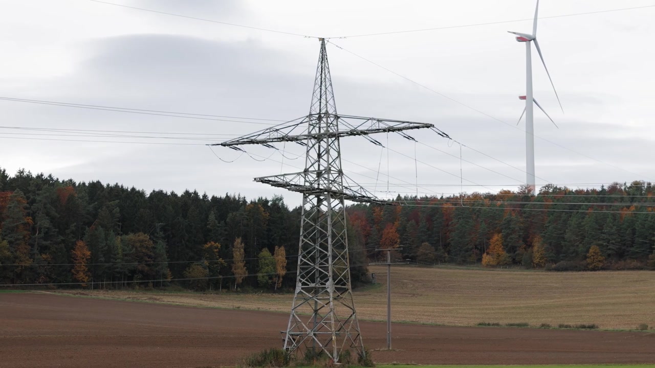 High-voltage transmission tower standing in an open rural field with autumn trees in the background