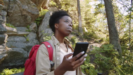 afro-american female tourist using smartphone in forest