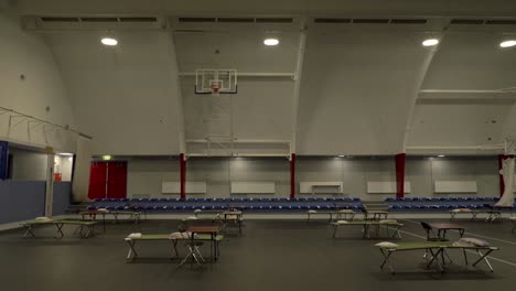 bed and table lined up in sports hall for emergency shelter during corona