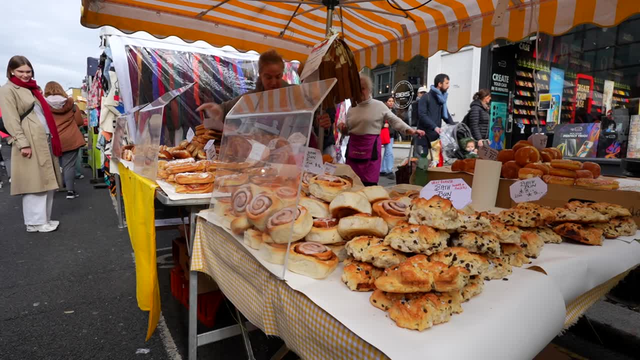 Tourist looks at cinnamon rolls and croissants at a pastry stall on Portobello Road Market in Notting Hill, London
