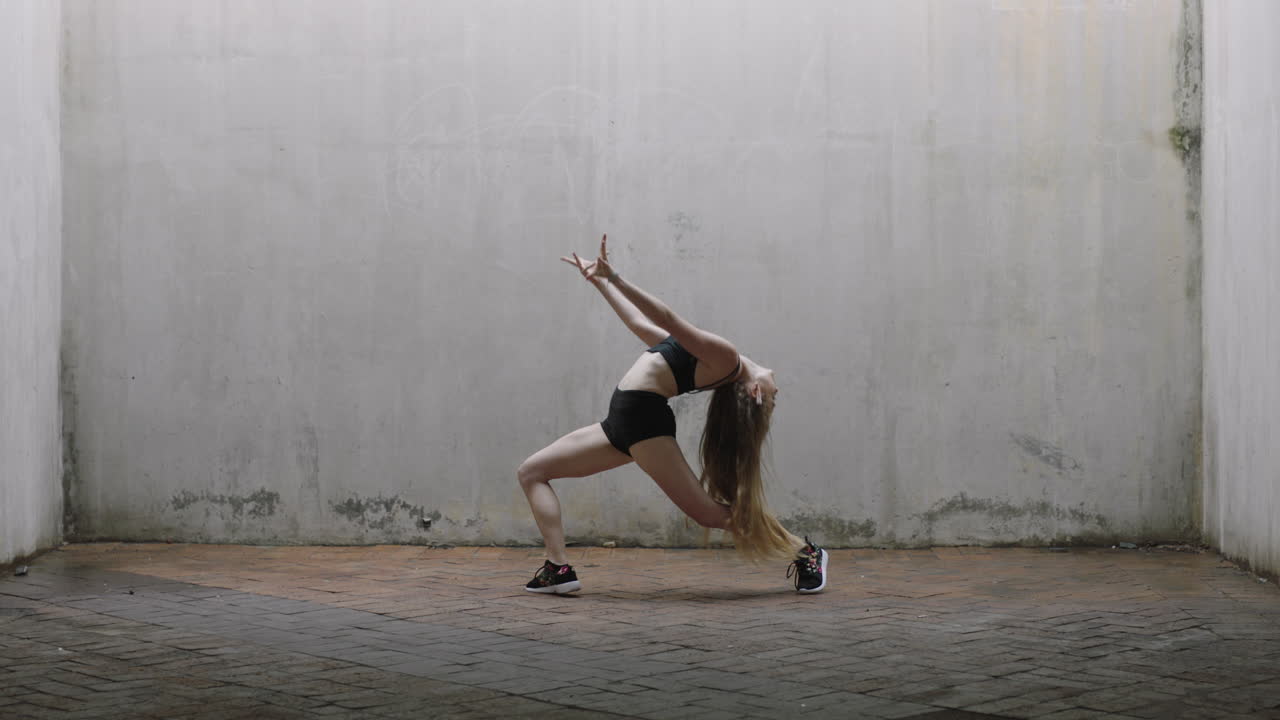 mujer bailarina atractiva joven bailarina de calle caucásica realizando movimientos contemporáneos disfrutando de la expresión de la danza moderna practicando en un almacén grungy