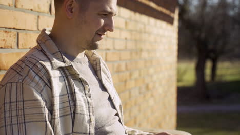 Close-up-view-of-caucasian-man-using-laptop-while-sitting-on-a-bench-outside-a-country-house