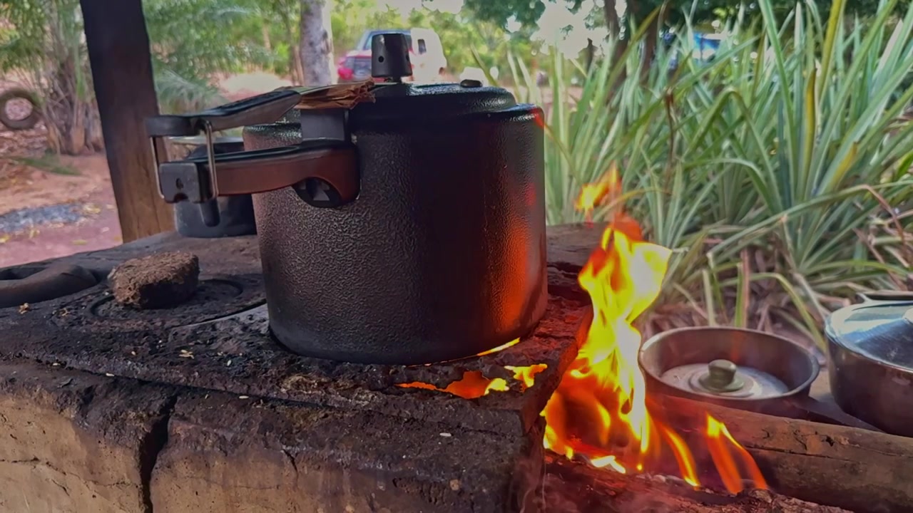 Slowmotion-nærbillede af en trykkoger, der opvarmes over et træbål på et rustikt udendørs komfur, der viser traditionel madlavning og off-grid madtilberedning.