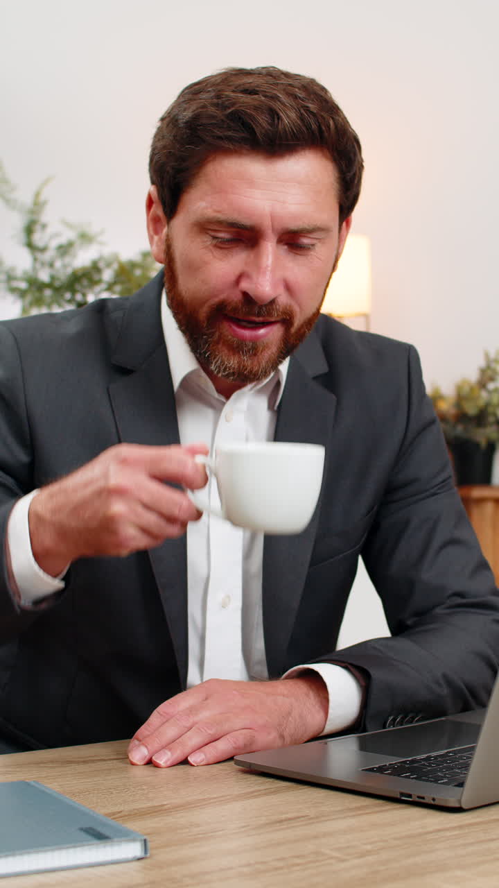 Midaldrende forretningsmand gaber, læner hovedet i hænderne, ryster sig selv, drikker stærk kaffe og vender tilbage til arbejdet